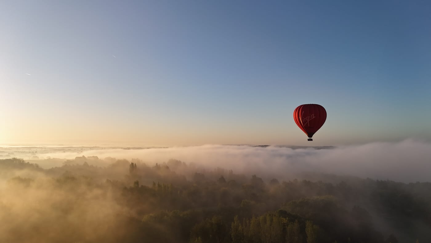 Virgin hot air balloon flying above misty countryside at sunrise