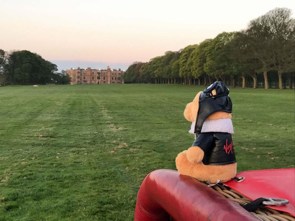 A teddy bear in a Virgin flying outfit overlooking a launch field and stately home at dusk