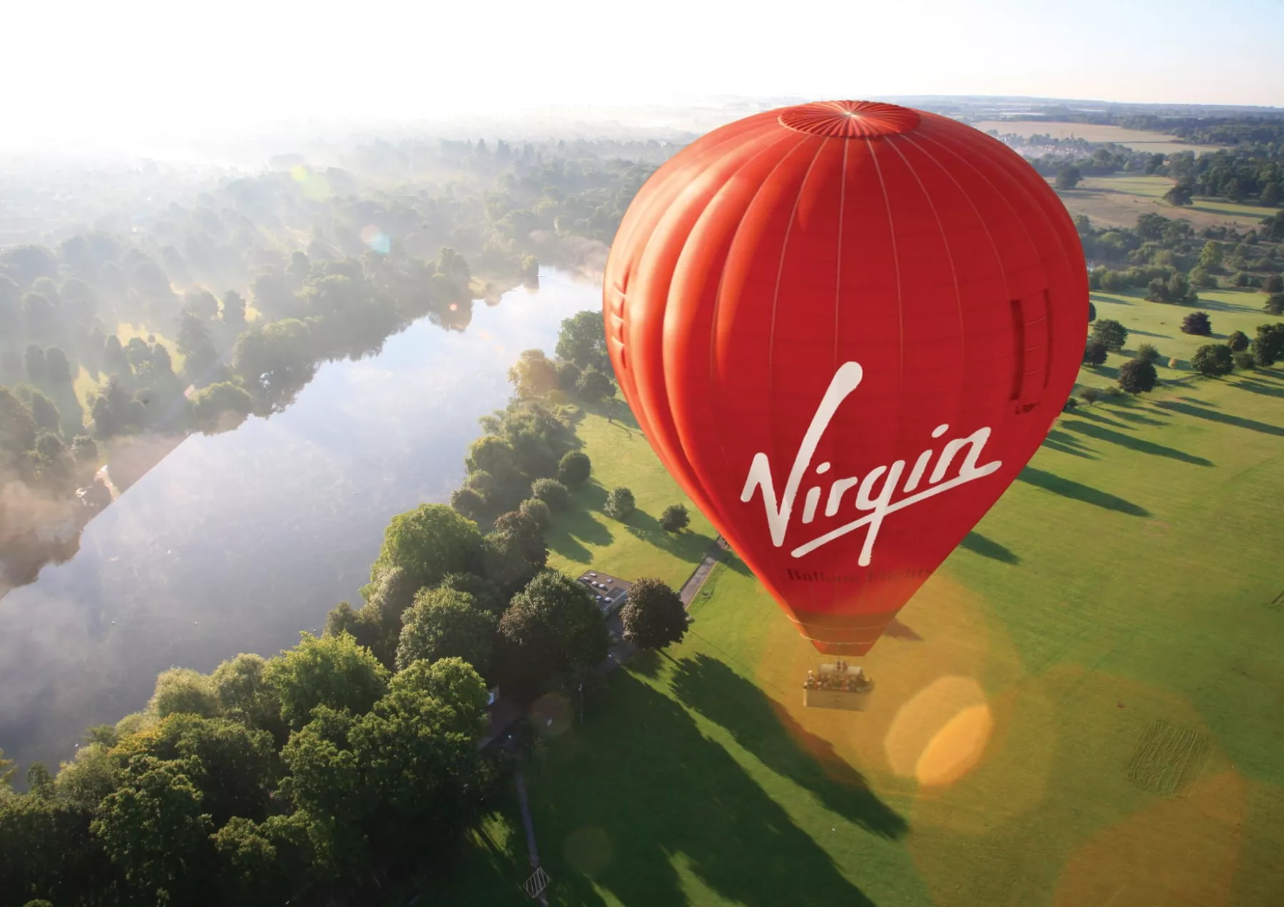 A Virgin hot air balloon rising over the river at Henley-on-Thames as the sun comes up