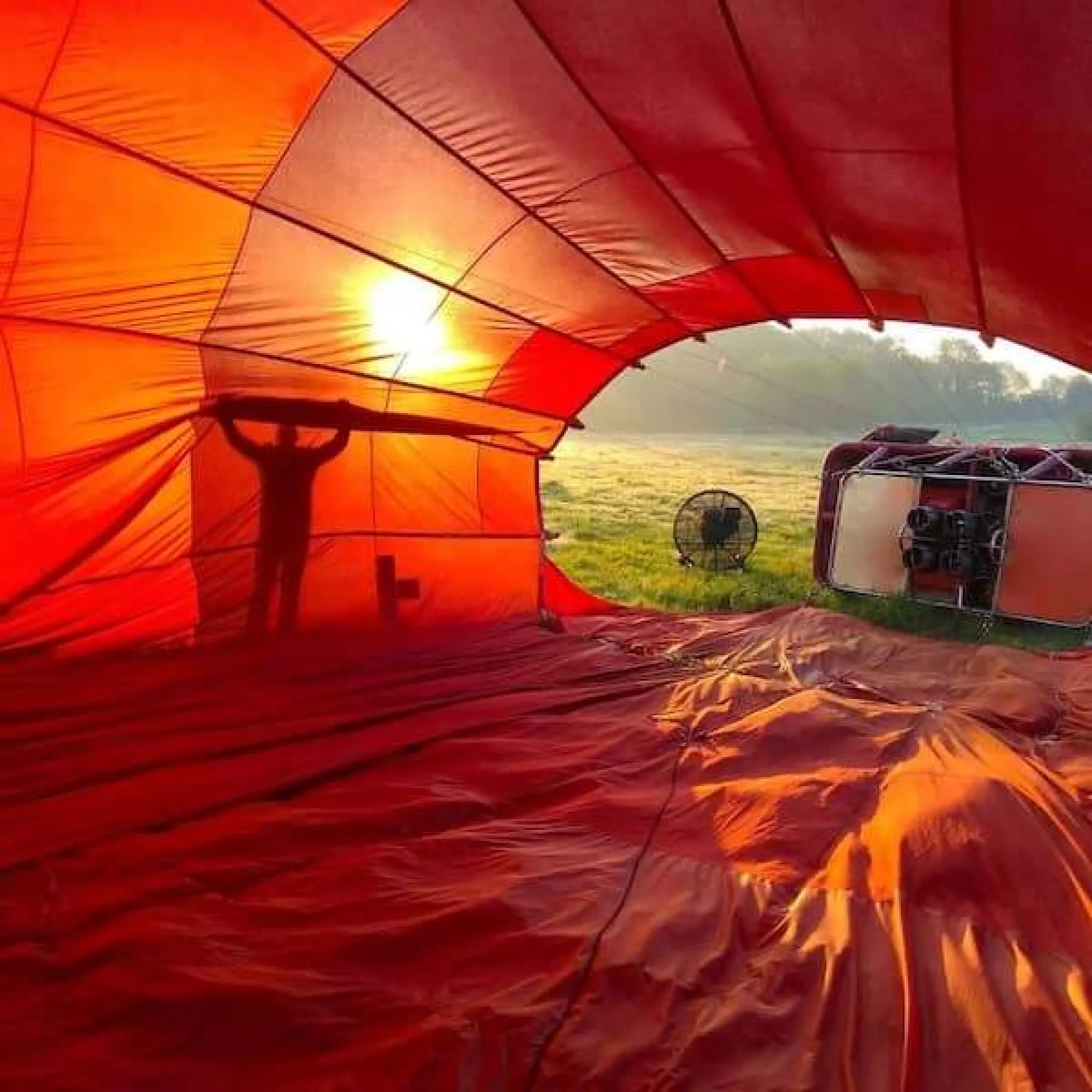 A view from inside a hot air balloon during cold inflation of a silhouette visible through the bright red balloon fabric lit up from the sun behind