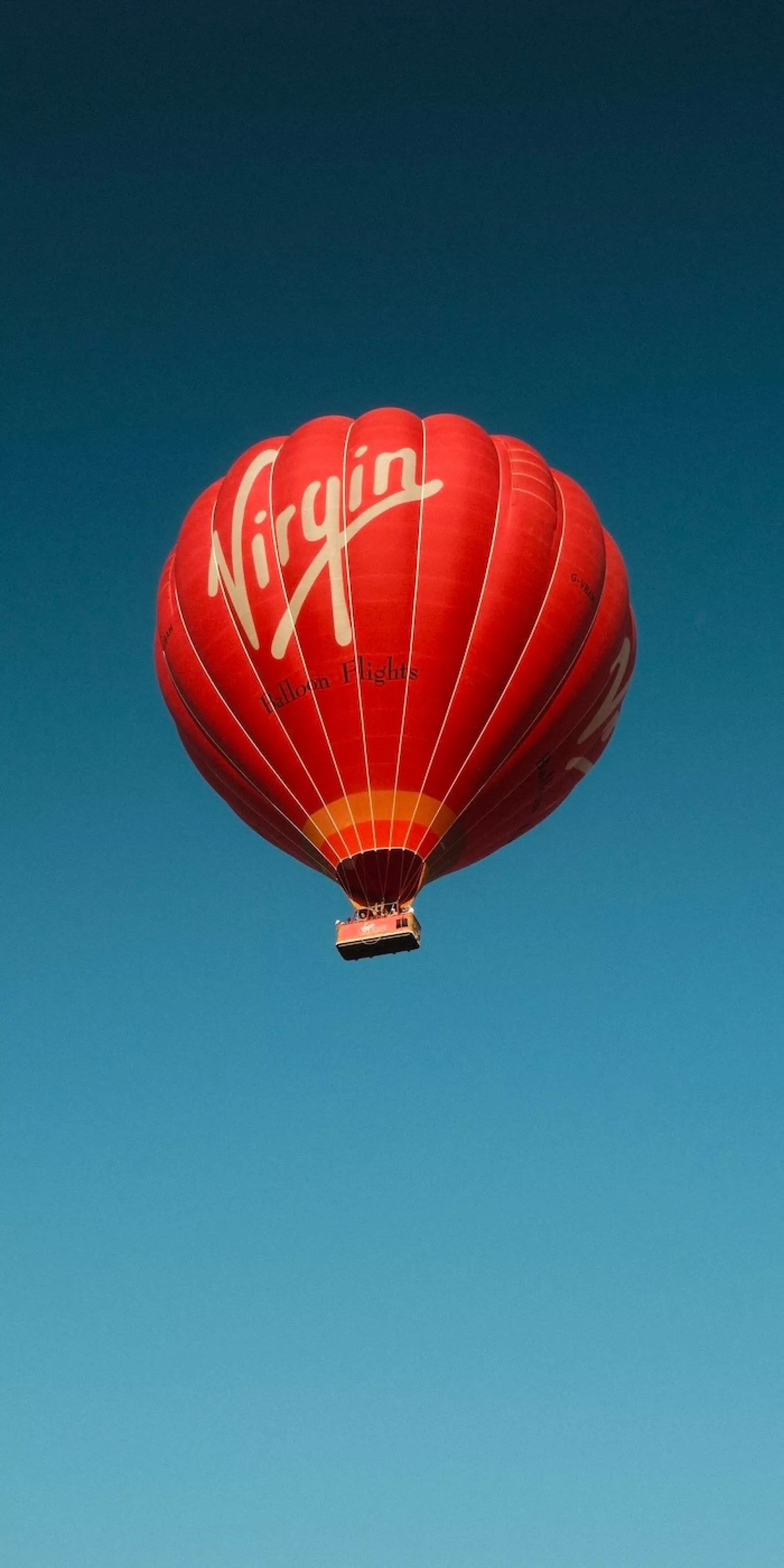 A red virgin hot air balloon flying into the deep blue sky